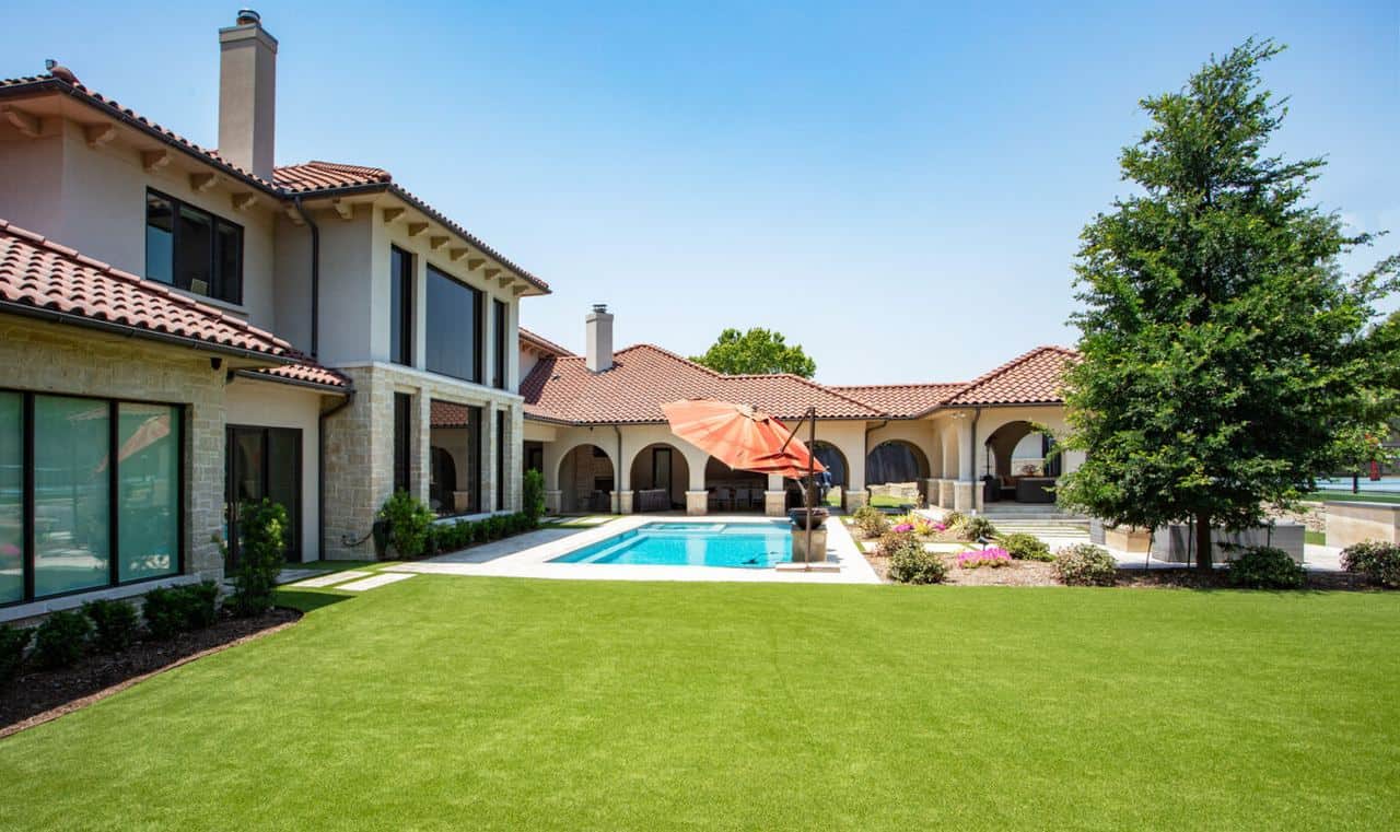Modern home with a red-tile roof, pool, and vibrant green artificial grass lawn, showcasing a low-maintenance yard design.