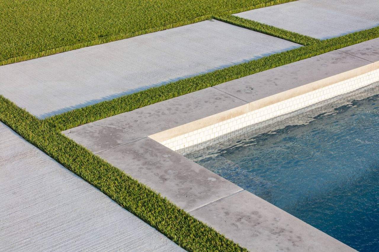 A poolside landscape shows artificial grass strips between concrete slabs, illustrating that synthetic turf can allow for water drainage around hardscapes.