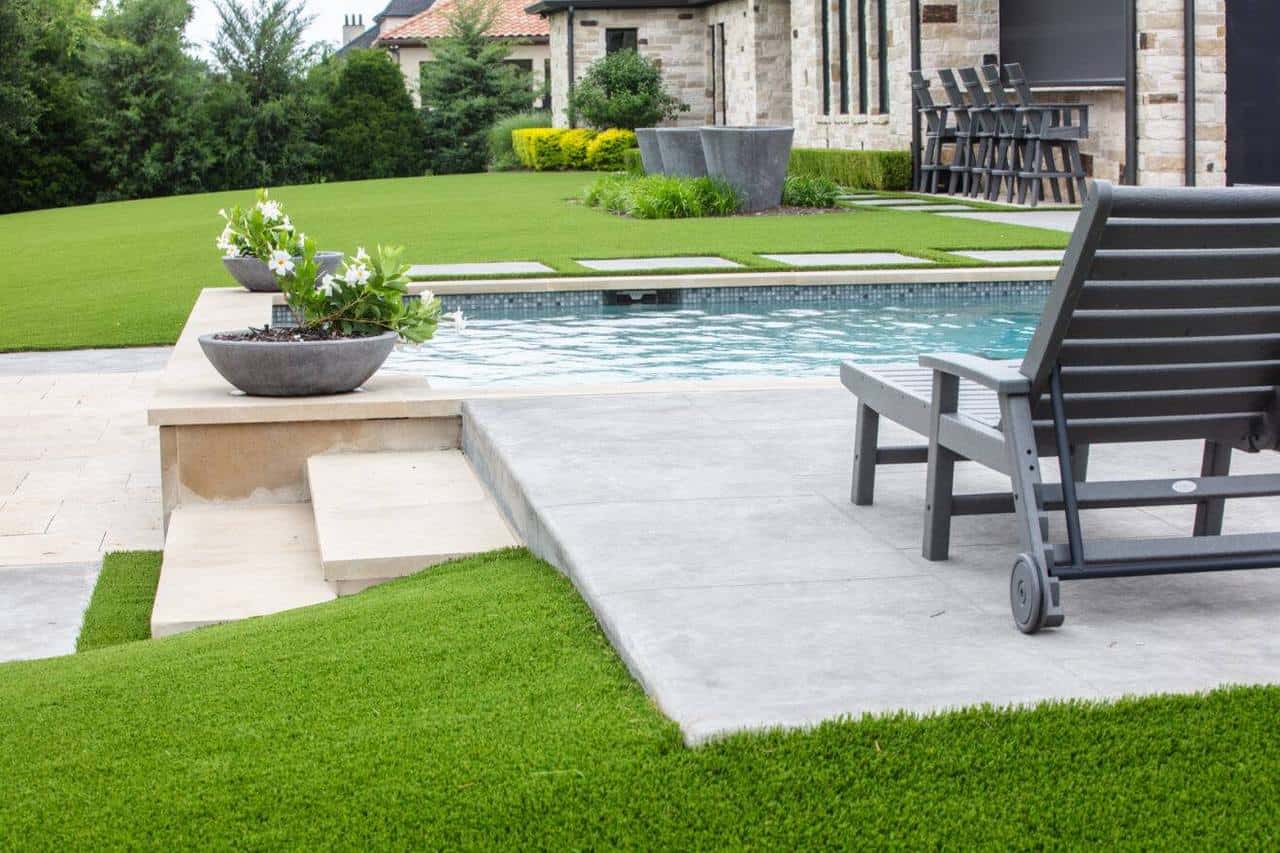 A luxurious backyard pool area with surrounding artificial grass shows no visible puddling, indicating well-designed drainage and installation.