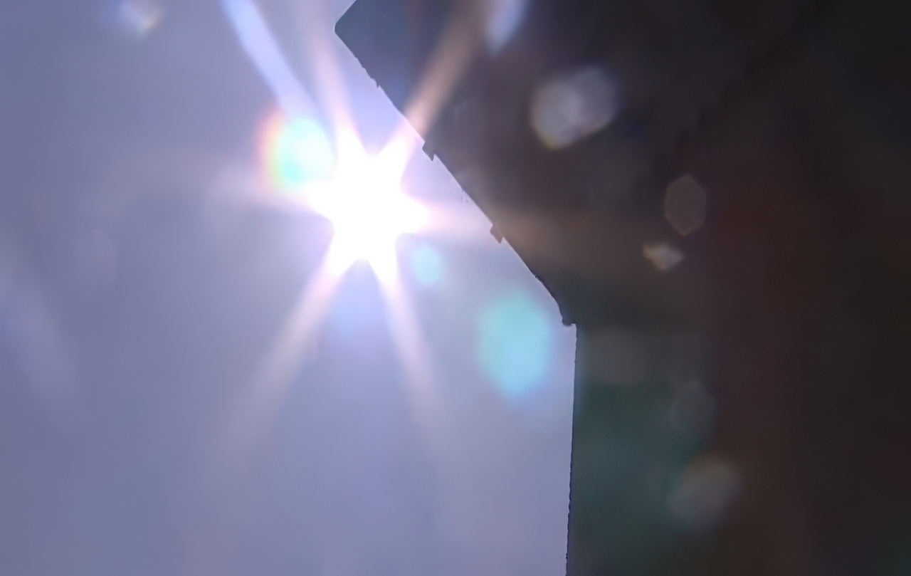 A bright midday sun reflects off a second-story window, creating intense glare and lens flare that can cause artificial grass to melt below.