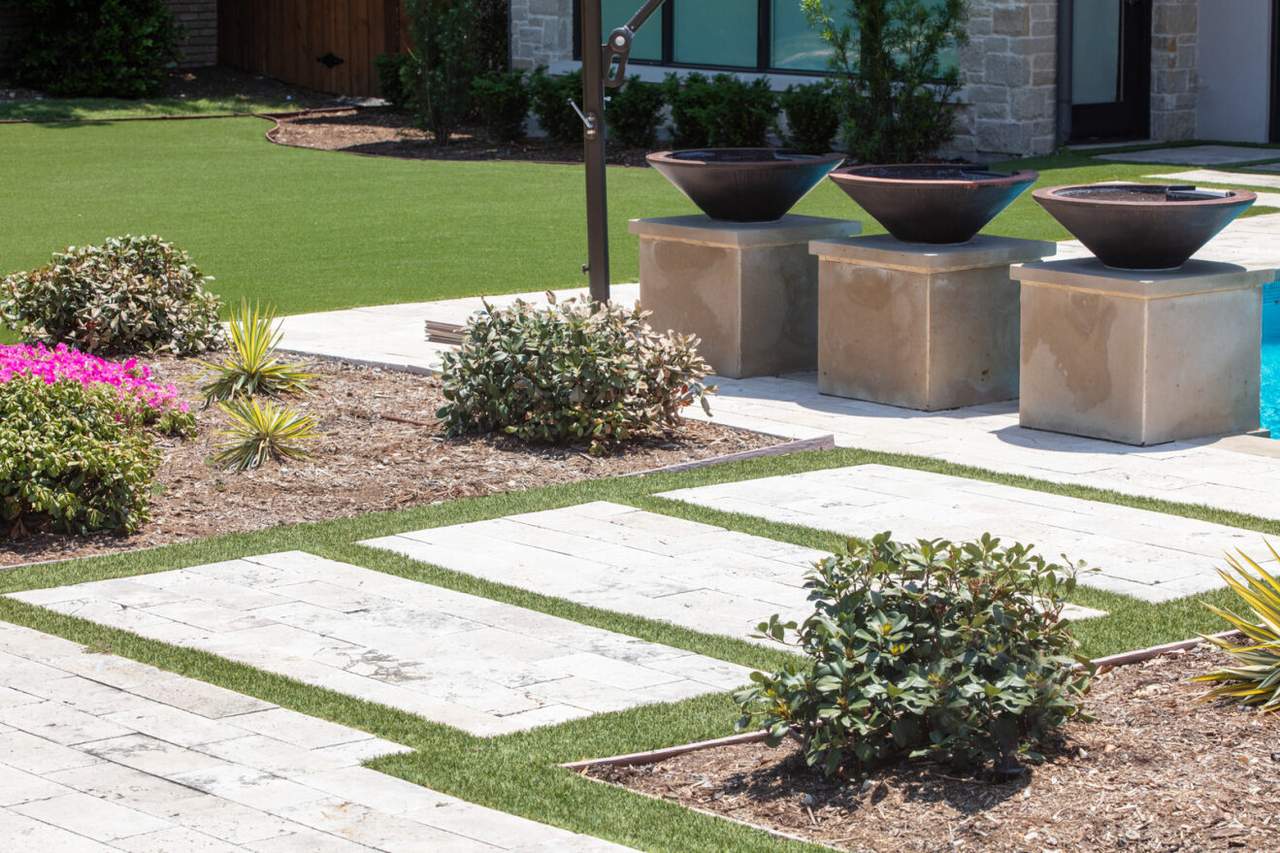 A backyard with artificial grass, stone pathways, and fire bowls sits in direct sunlight, highlighting areas vulnerable to glare-induced melting.