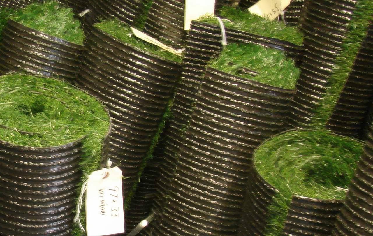 Rolls of artificial turf stacked vertically, showcasing green blades and black backing with eco-friendly material tags.