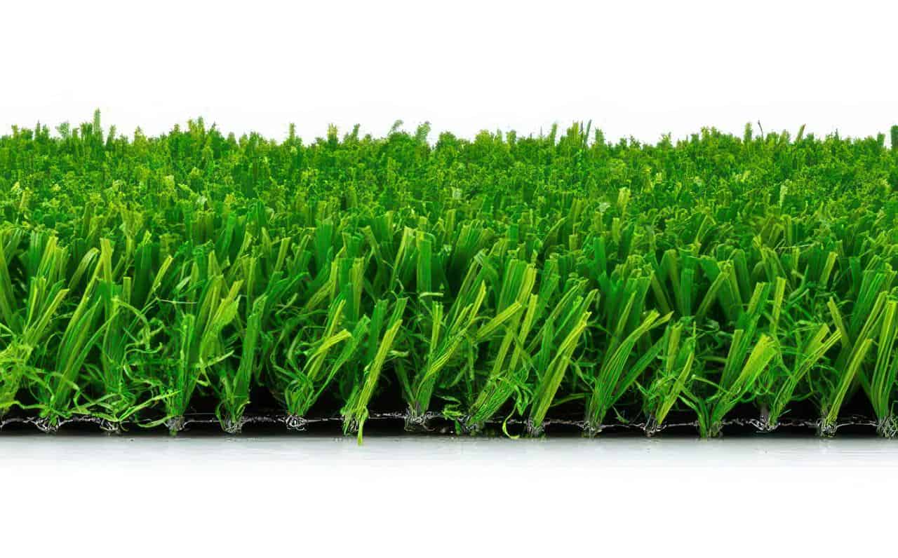 Side view of artificial turf showing dense green blades and varied pile height on a flat white surface to highlight texture.