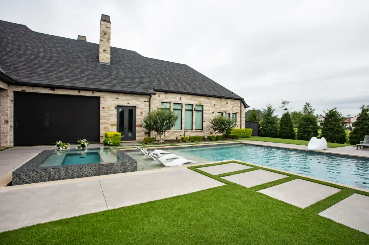 Synthetic turf backyard around a pool and hot tub with stepping stone pavers in Dallas Fort Worth