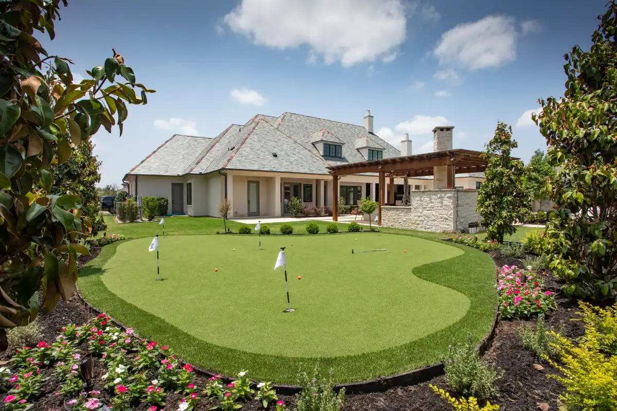 Artificial turf putting green with fringe and flower beds in a Dallas Forth Worth residential backyard