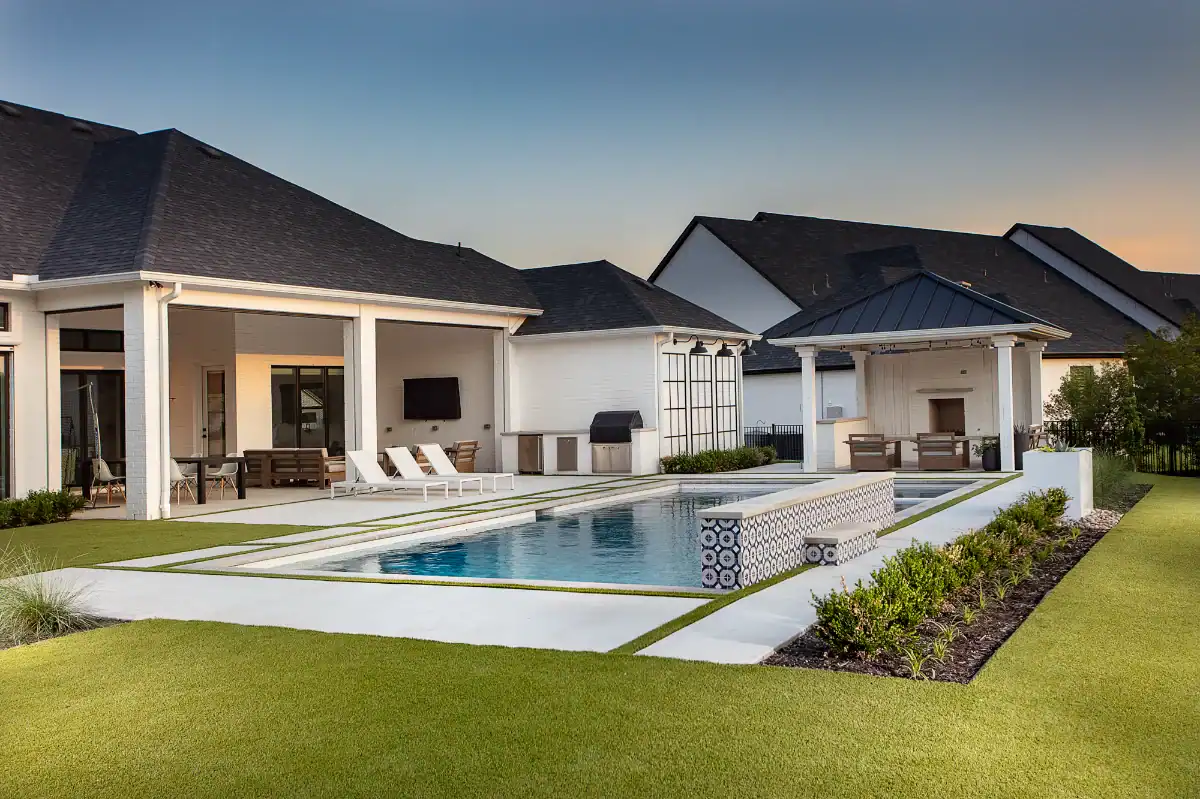 A large green artificial turf lawn in a residential backyard in Dallas Fort Worth around a spacious pool with a patio