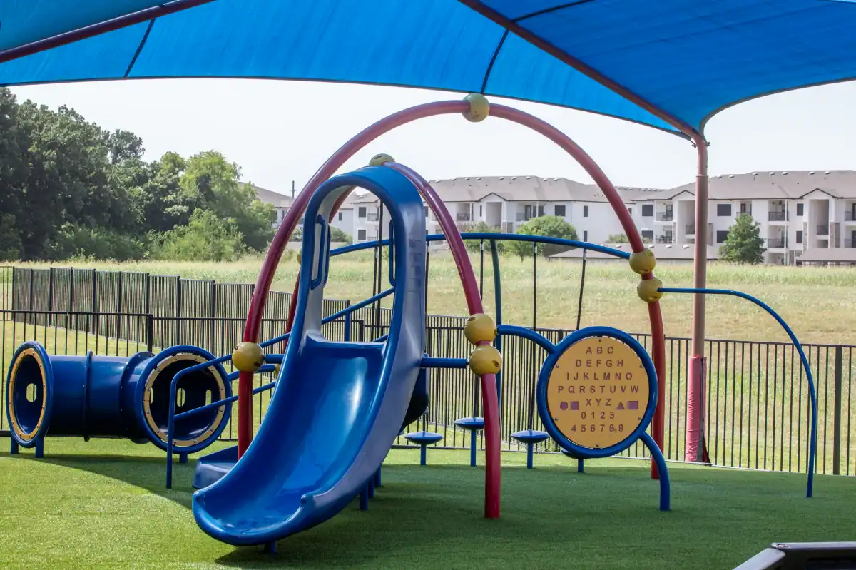 Artificial turf playground with play equipment and padding outside a school in Dallas Fort Worth