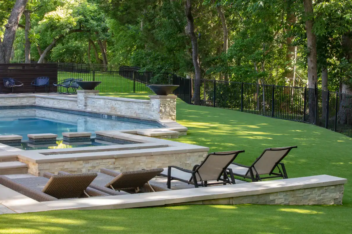 Pet Turf Surrounding Pool Shaded synthetic pet turf backyard with a pool and hot tub surrounded by trees